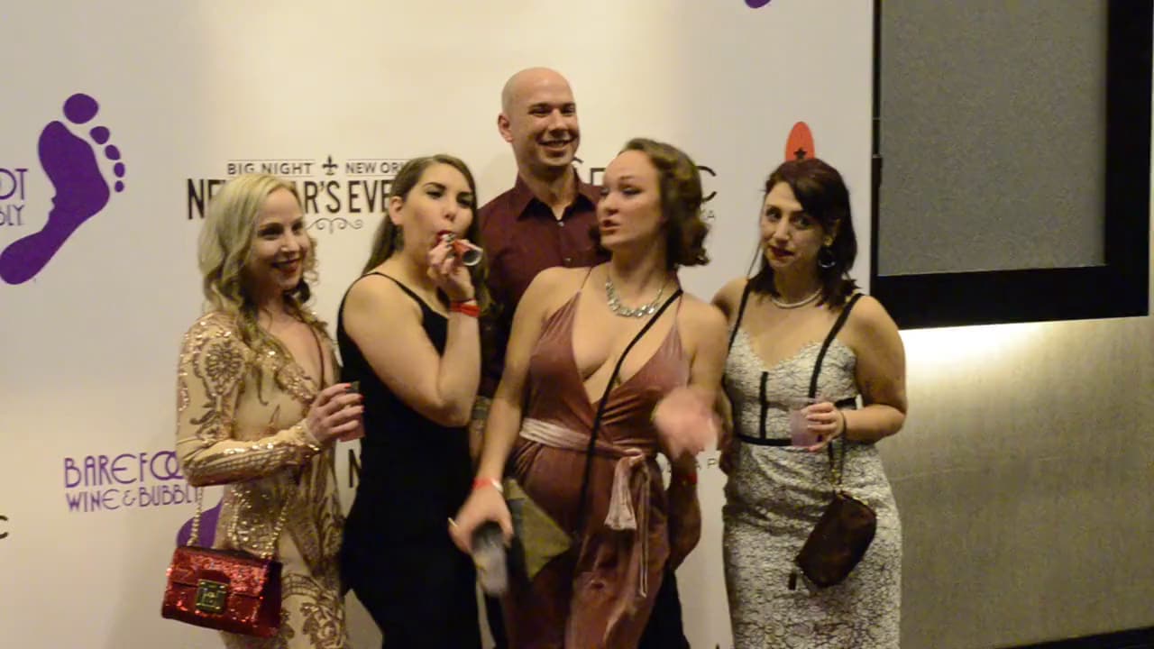 Five guests laughing together on the red carpet at a New Year's Eve gala sponsor wall.