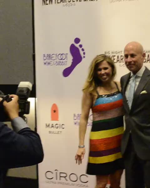 A photographer shoots a couple on the red carpet at a New Year's Eve gala sponsor wall.