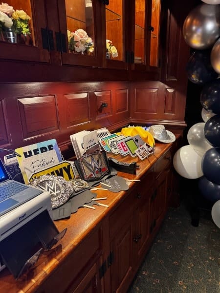 A props table with signs, hats and championship belts beside the booth's photo printer.