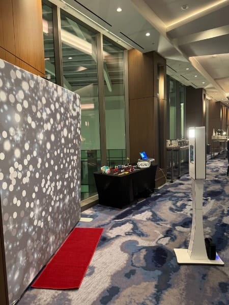 A silver sparkle backdrop, red carpet, props table and kiosk set up along a hotel corridor.